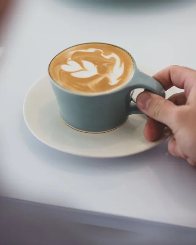A cappuccino with latte art in a blue-grey cup, held over a white saucer.