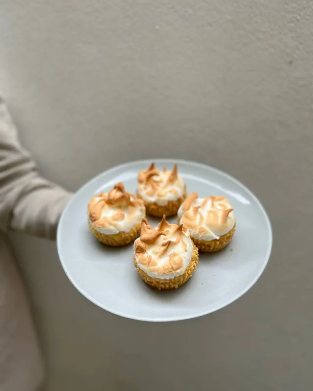 Four small meringue tarts on a white plate, held in one hand.